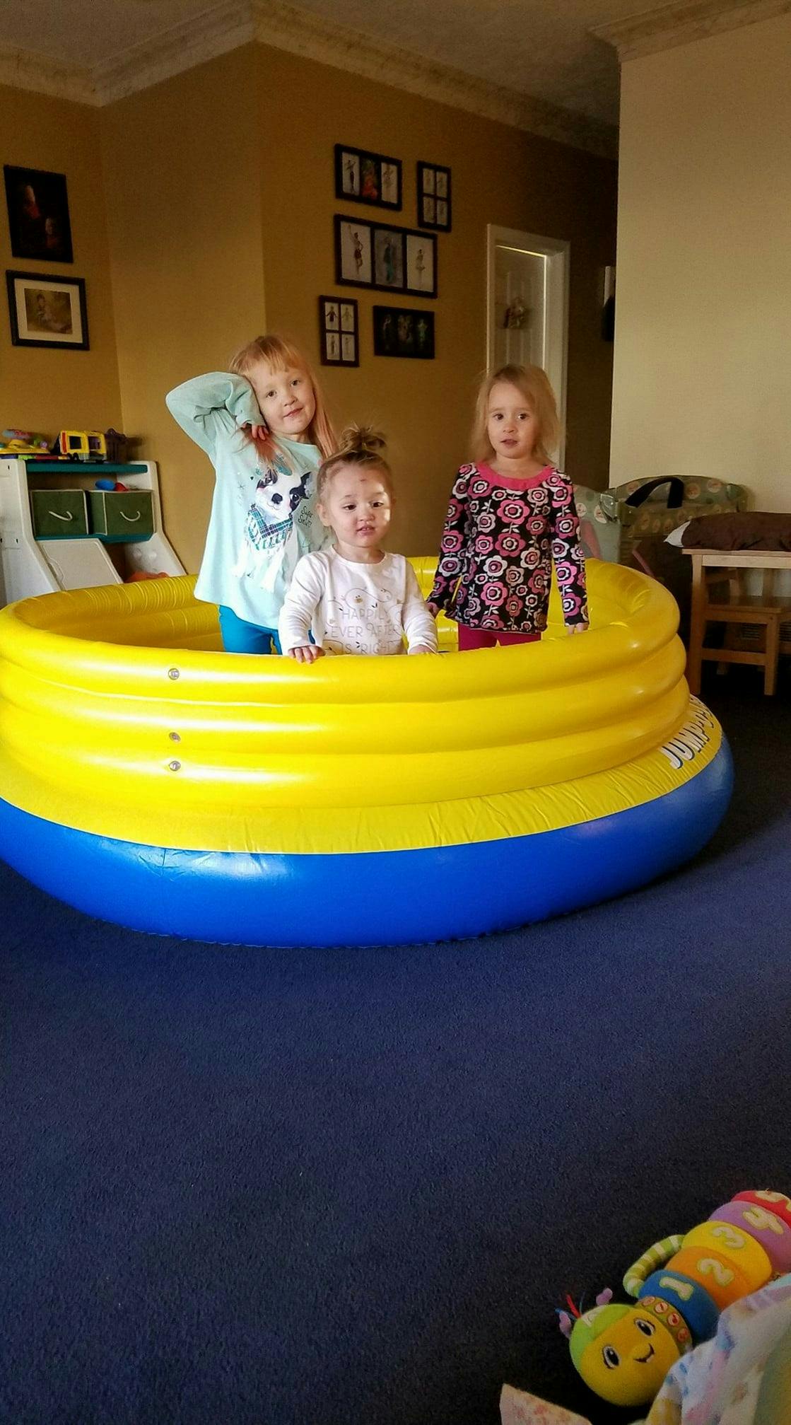 Three children standing in a yellow and blue inflatable pool indoors
