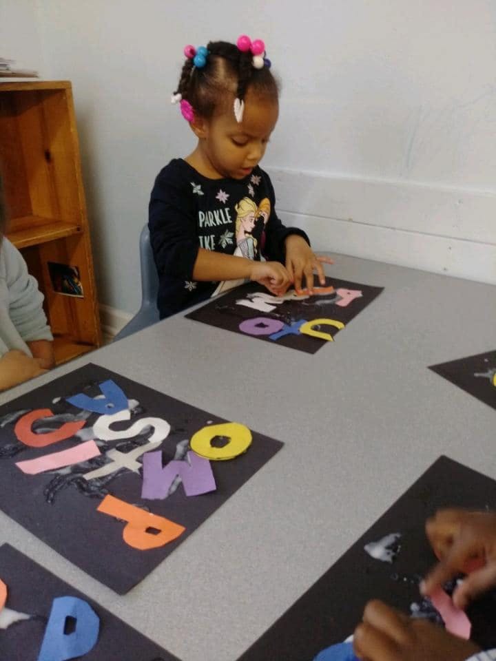 Child at a table arranging colorful letter cutouts on a black sheet