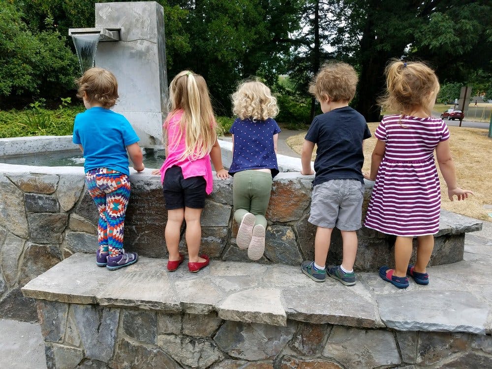 Five children standing on a stone ledge looking into a fountain