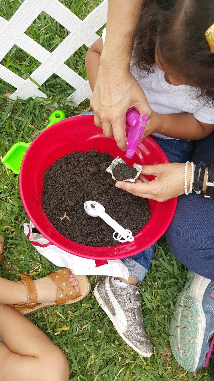 Person and child planting in a red bowl of soil