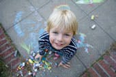Child looking up from drawing with chalk on pavement
