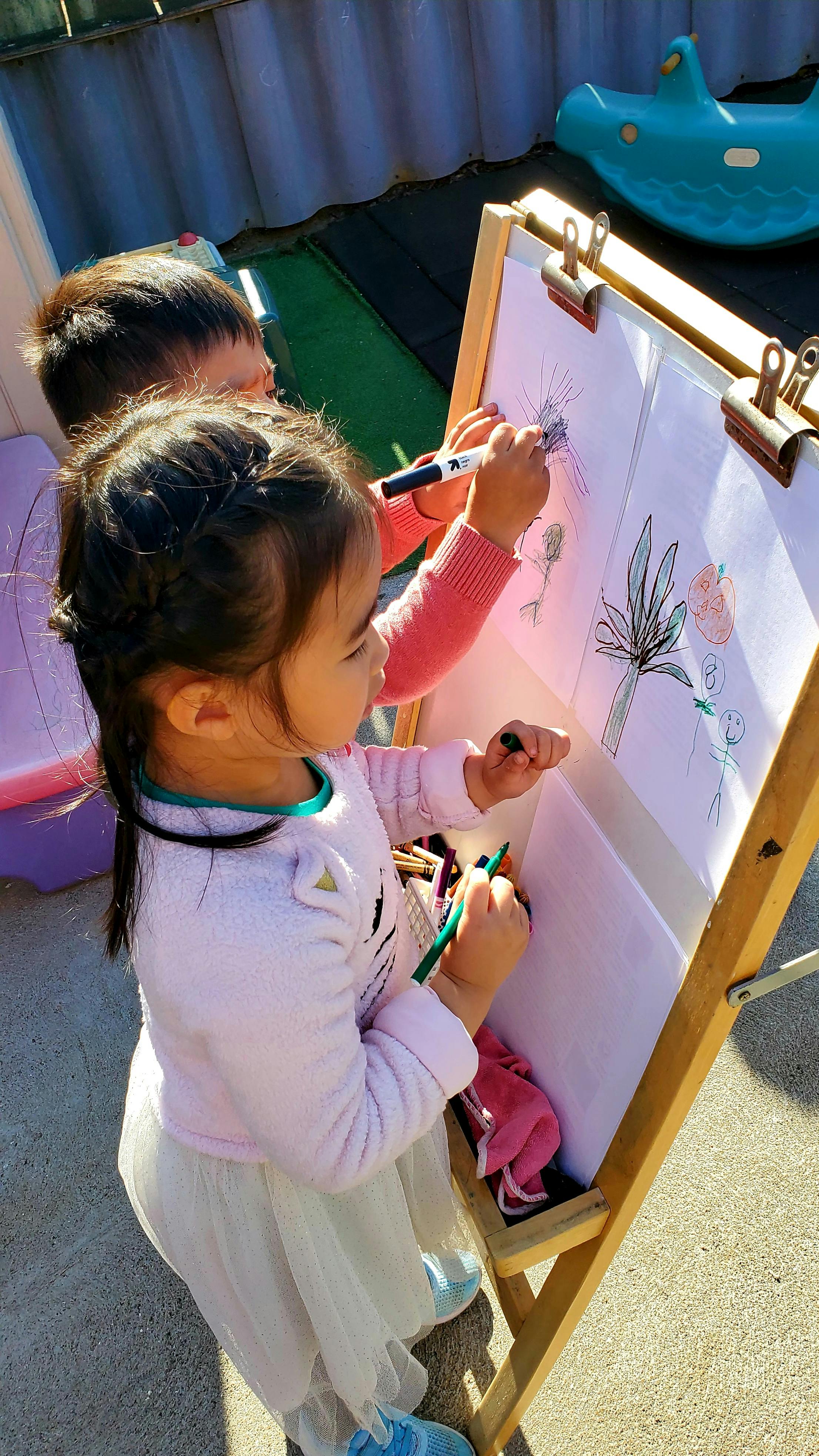 Two children drawing on an easel outdoors