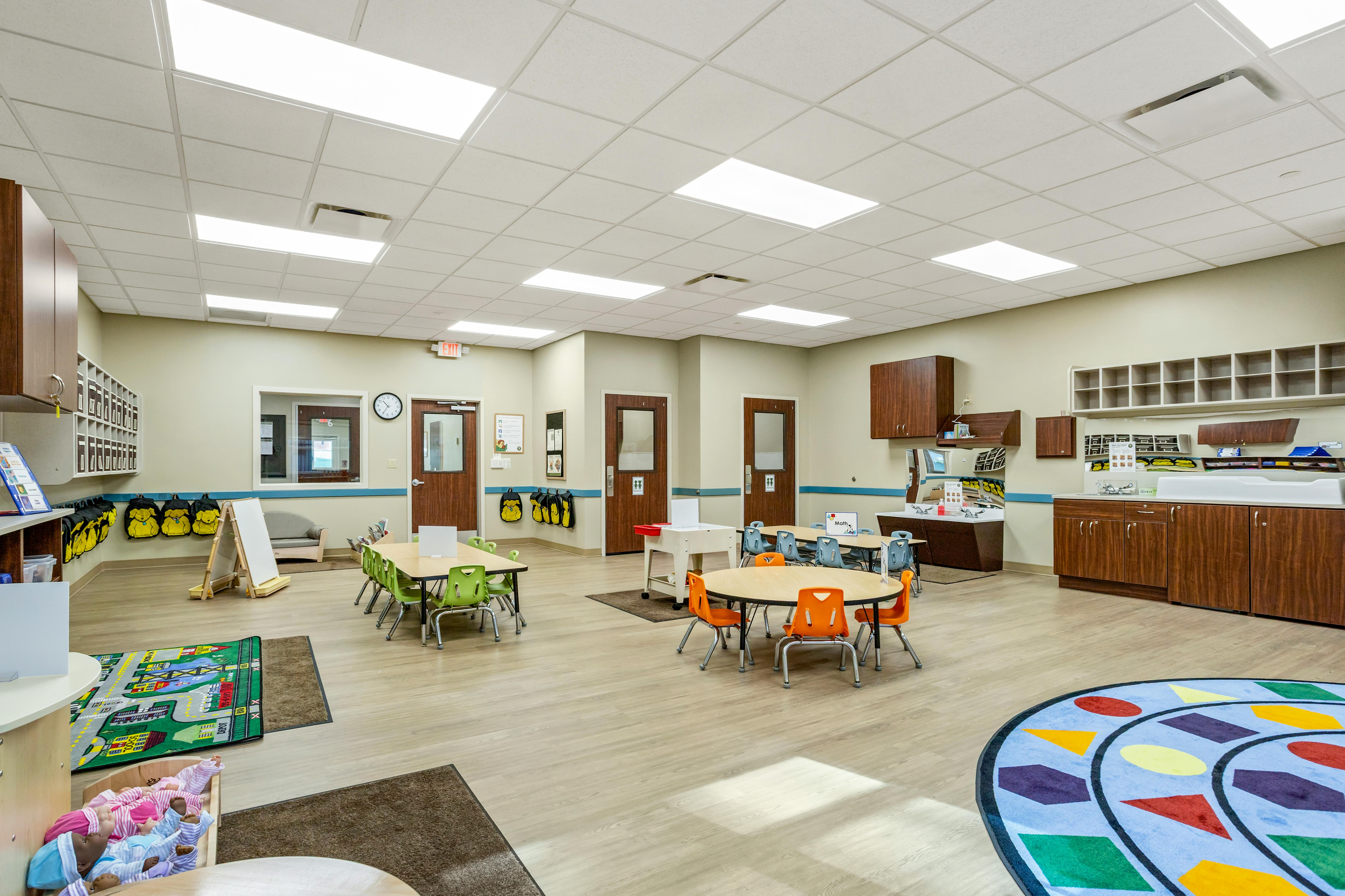 Classroom with child-sized tables and chairs, play mats, and storage