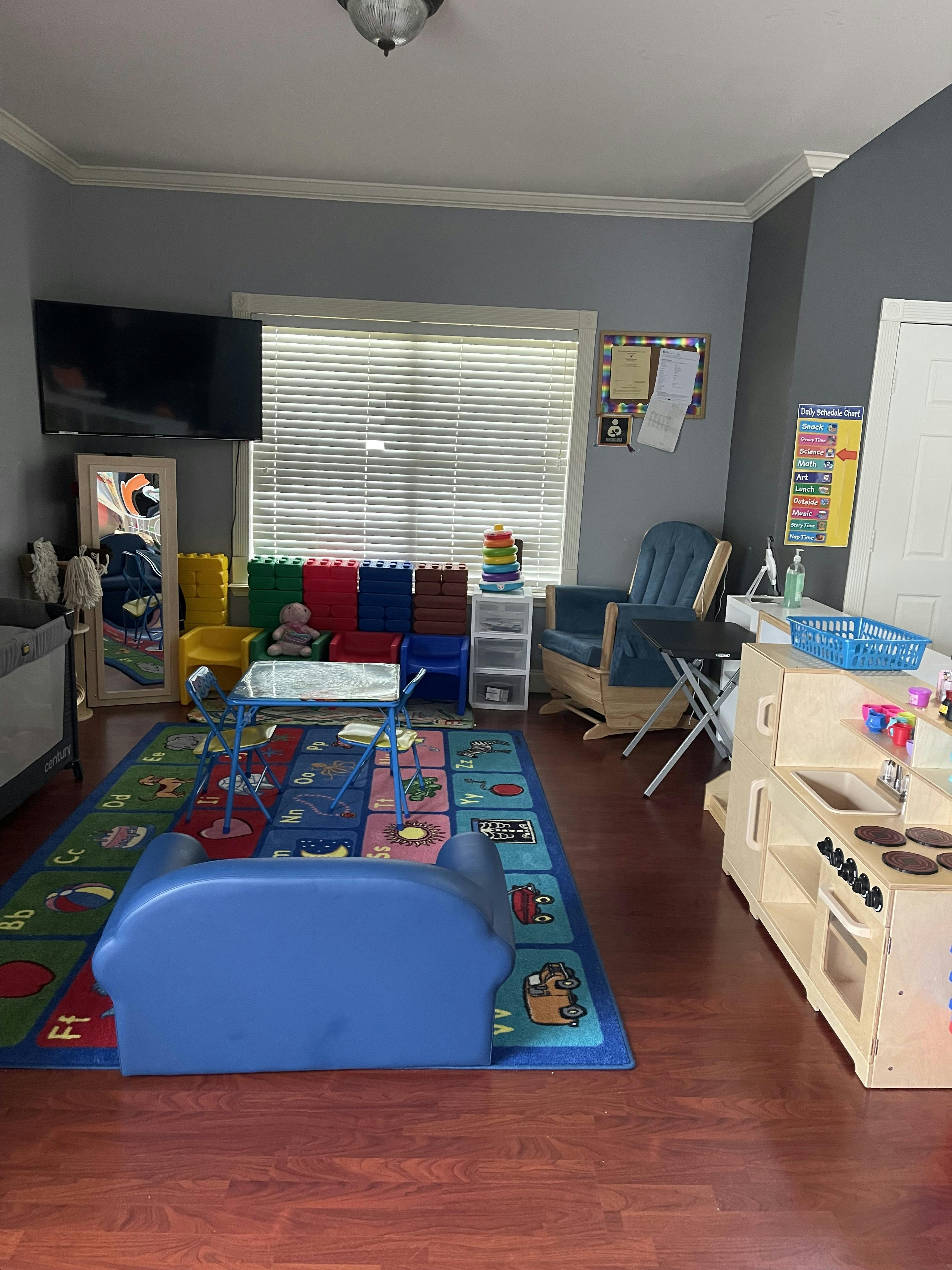 Childcare playroom with small tables, chairs, toys, and an alphabet rug