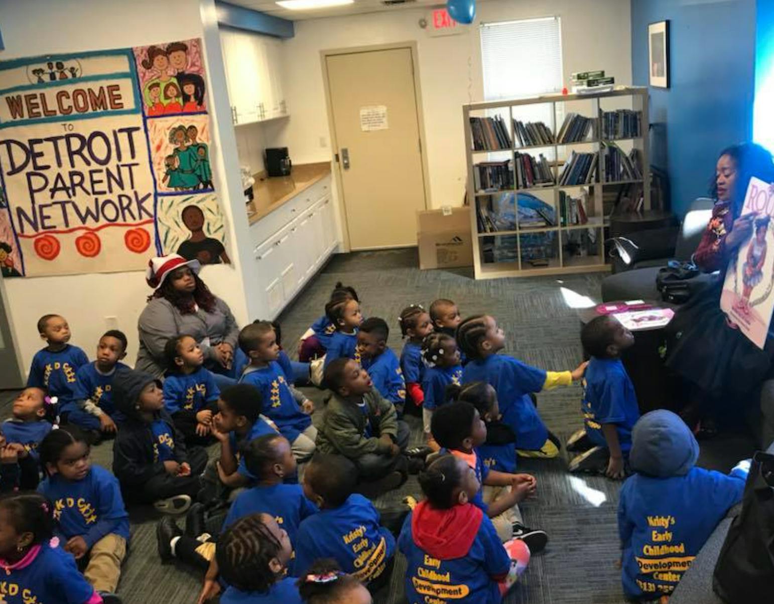 Adults and children sitting on the floor looking forward