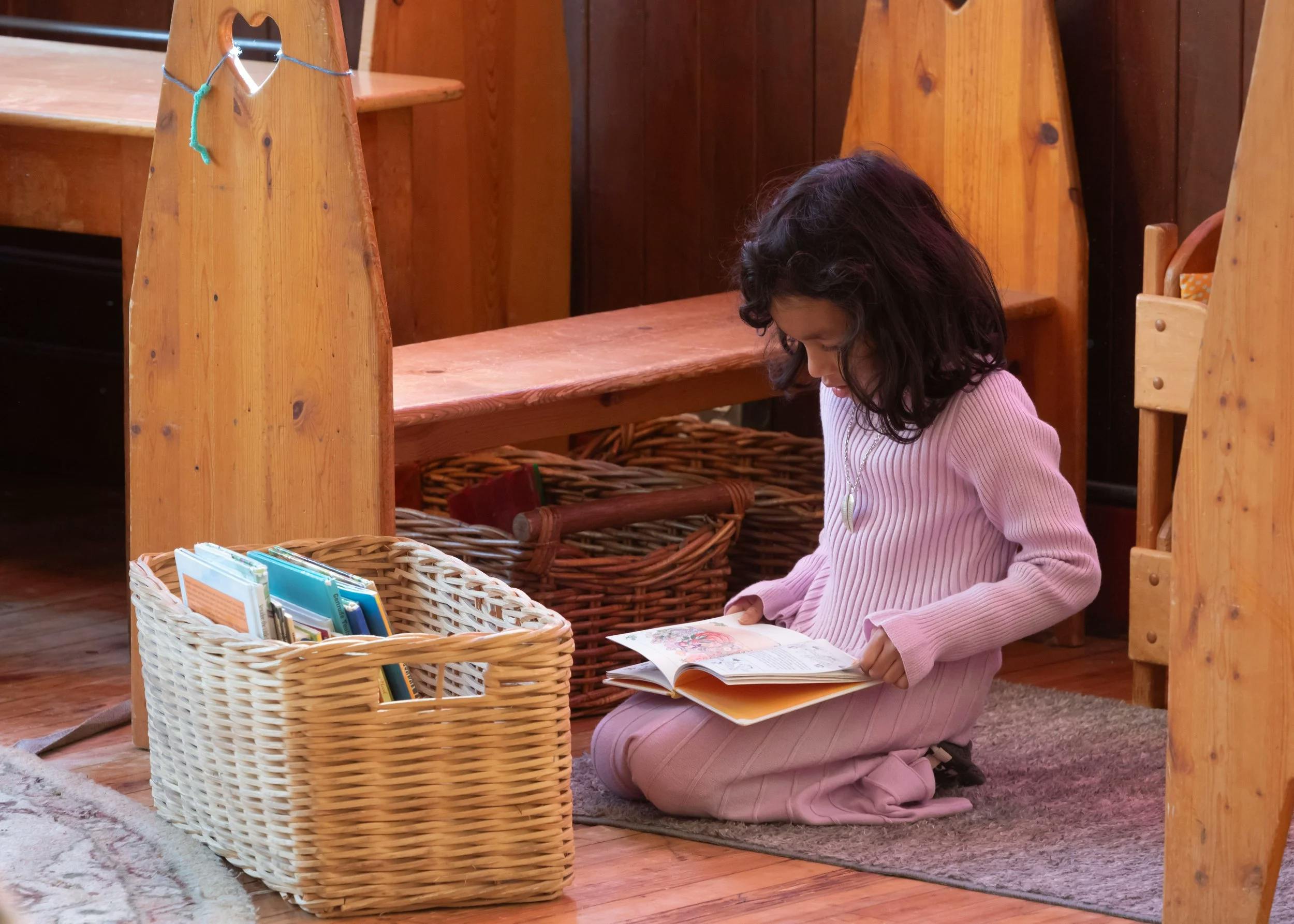 Child kneeling on a rug, reading a book in a classroom