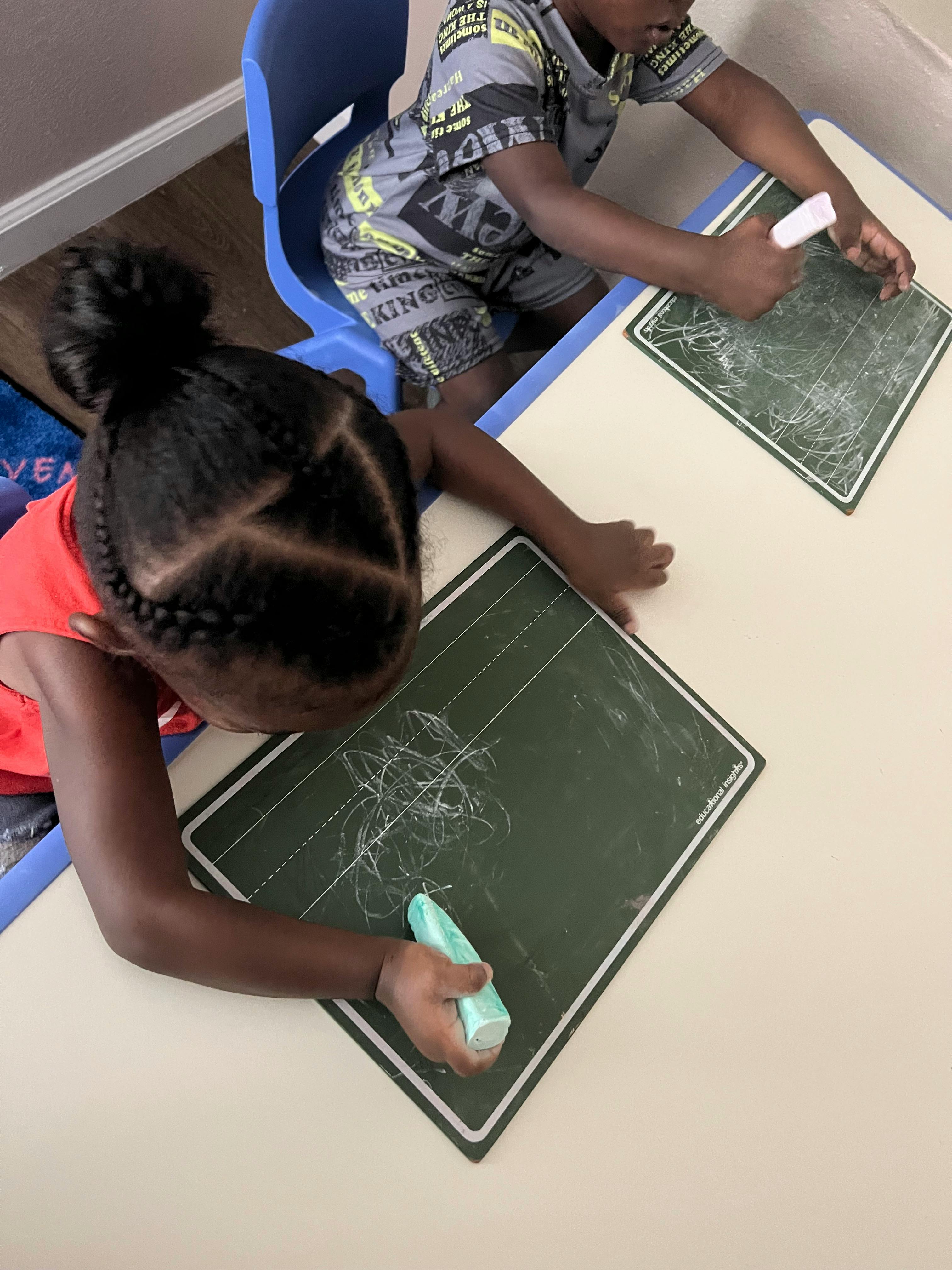 Two children drawing on chalkboards at a table