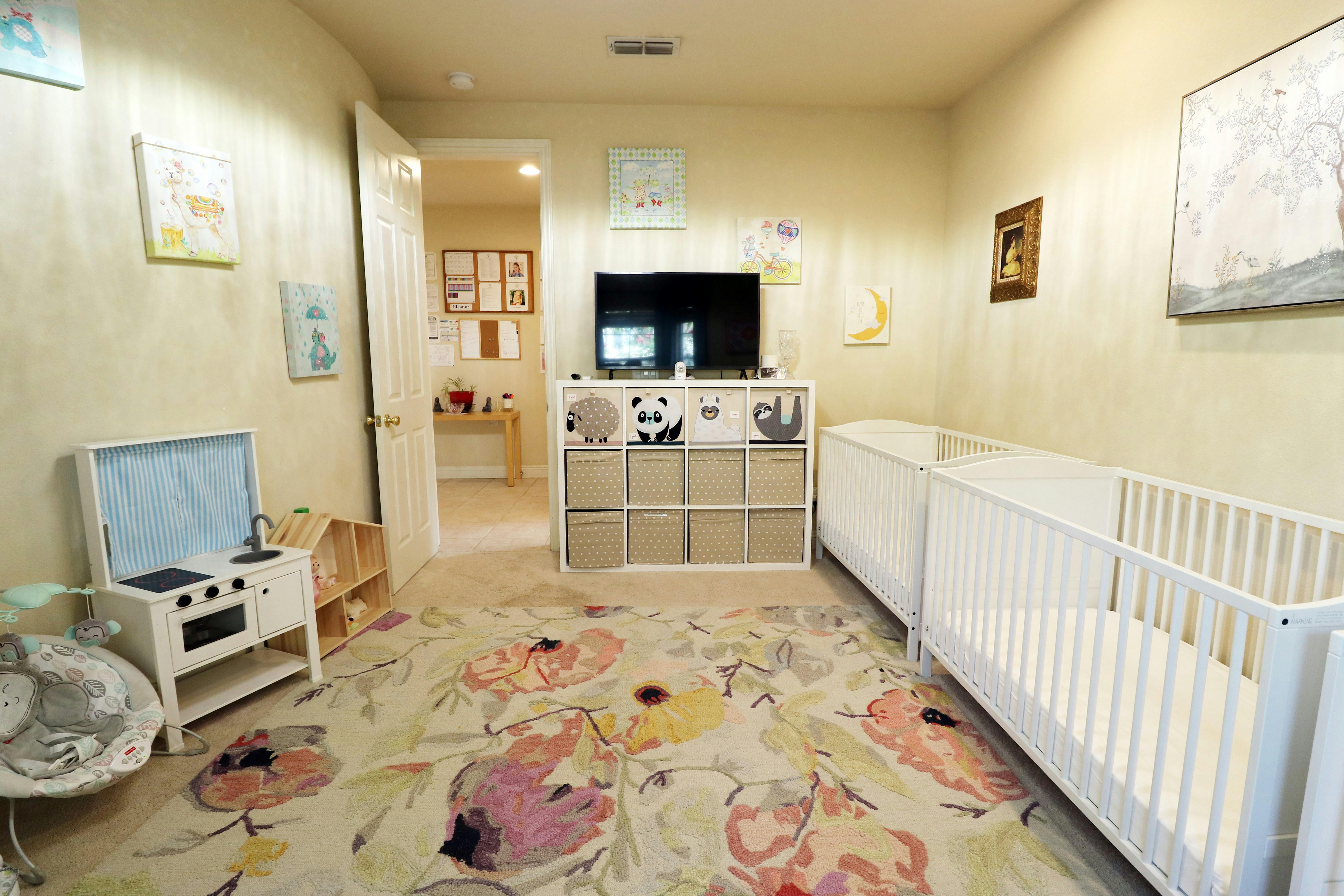 Room with two cribs, a television, and a toy kitchen