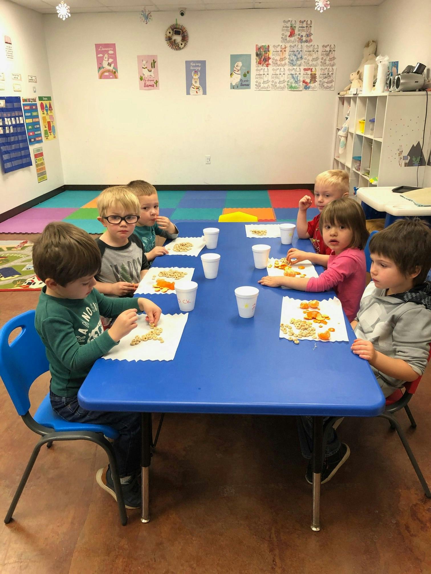 Children sitting at a blue table with snacks and eating snacks
