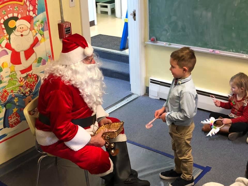 Person dressed as Santa Claus sitting with a child standing in front