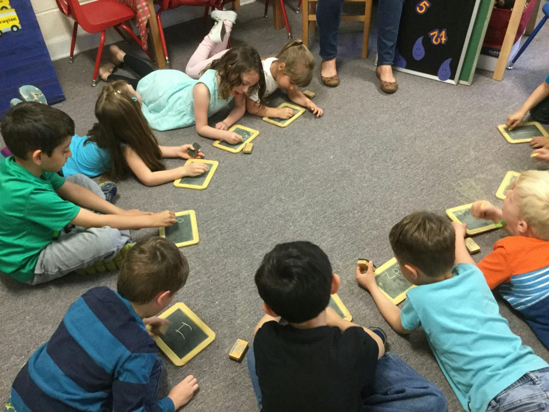 Children sitting on the floor drawing on small chalkboards
