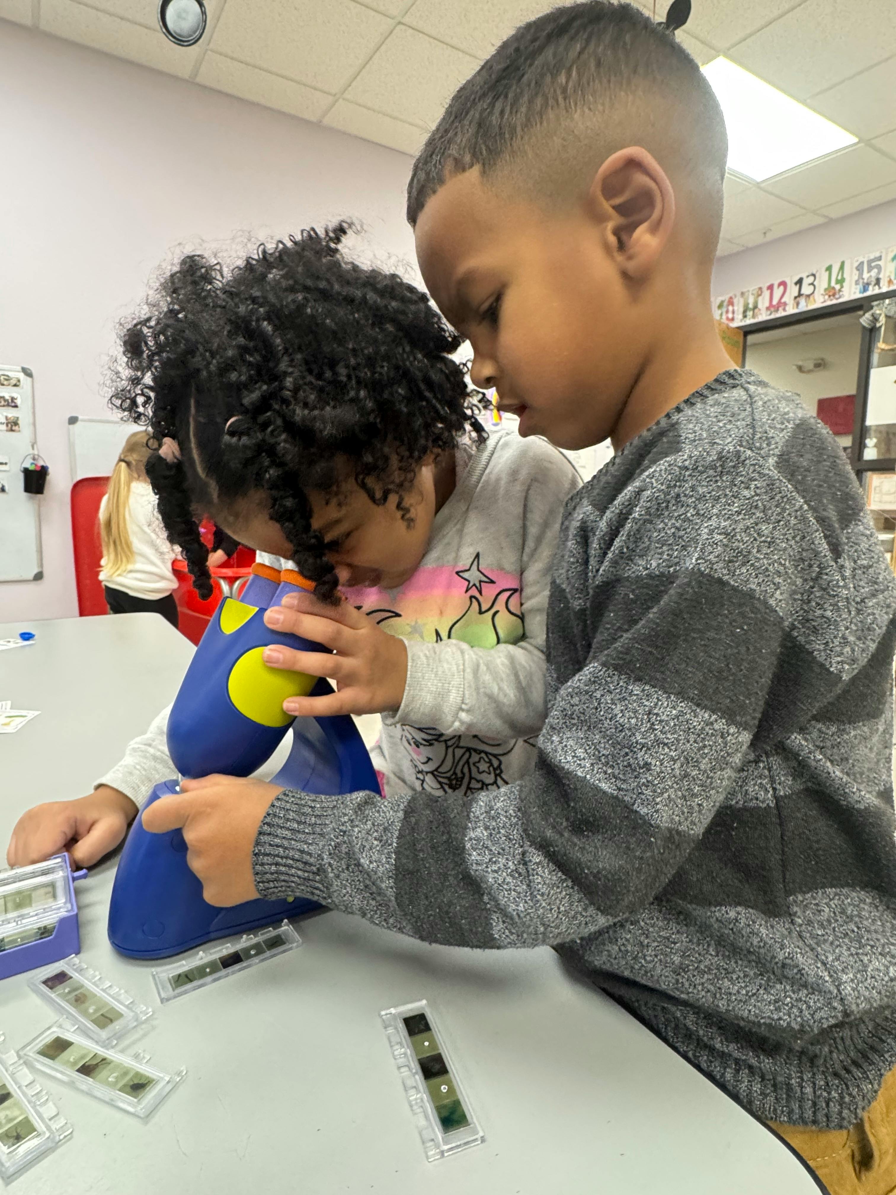 Two children looking into a blue microscope on a table