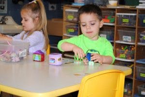 Child playing with blocks at a table, another child in background