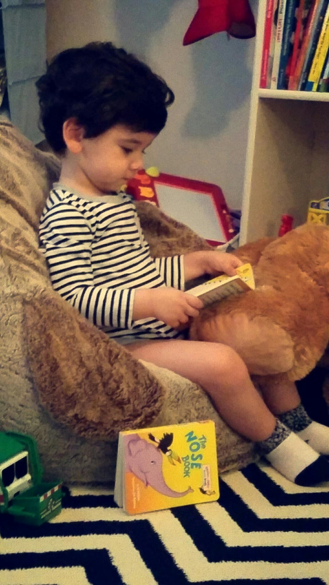 Child in striped shirt reading a book while sitting on a beanbag chair