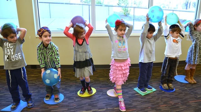 Children balancing on boards while holding balls
