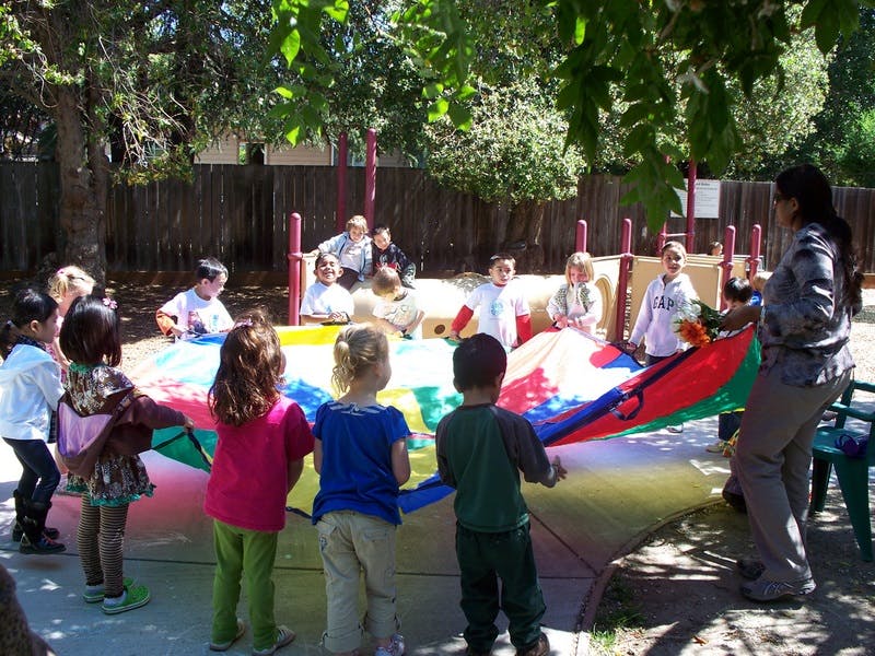 Children and an adult playing with a colorful parachute outdoors