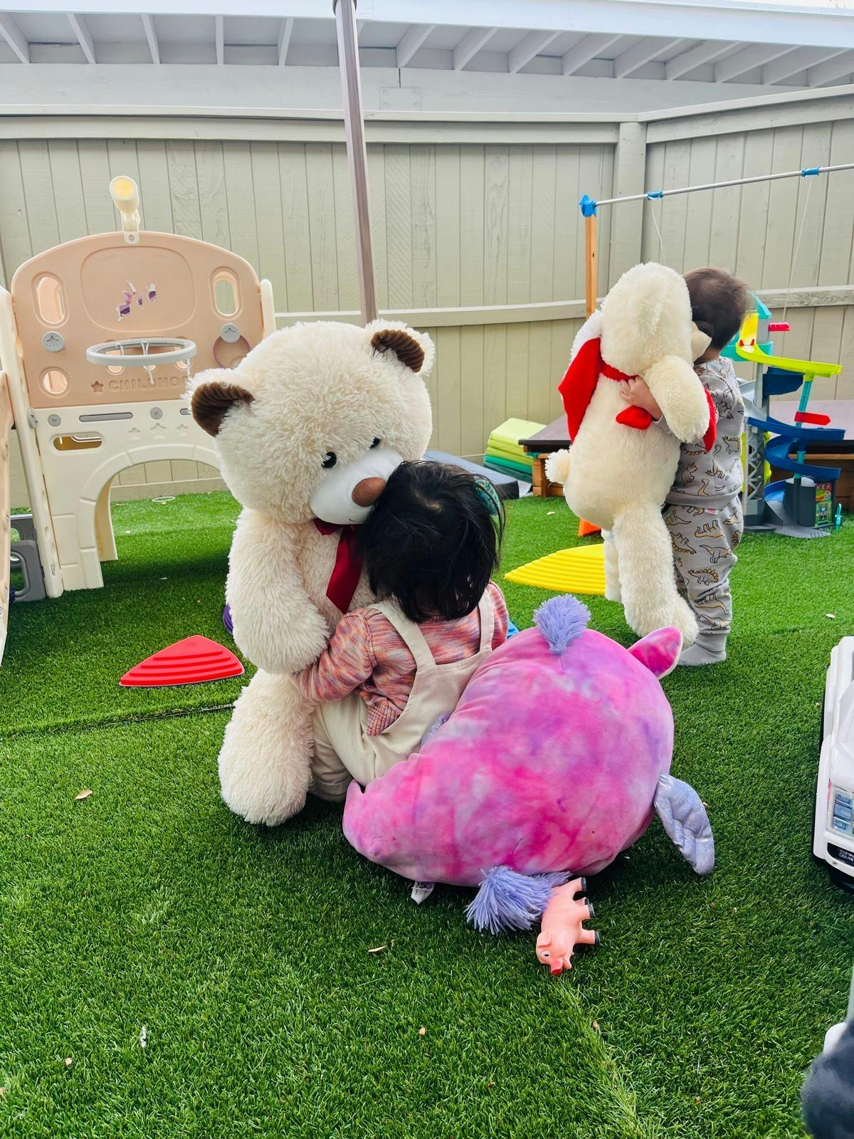 Child hugging a large teddy bear, another child holding a stuffed animal