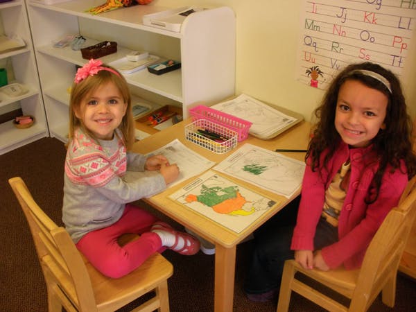 Two children sitting at a table with drawings in a classroom