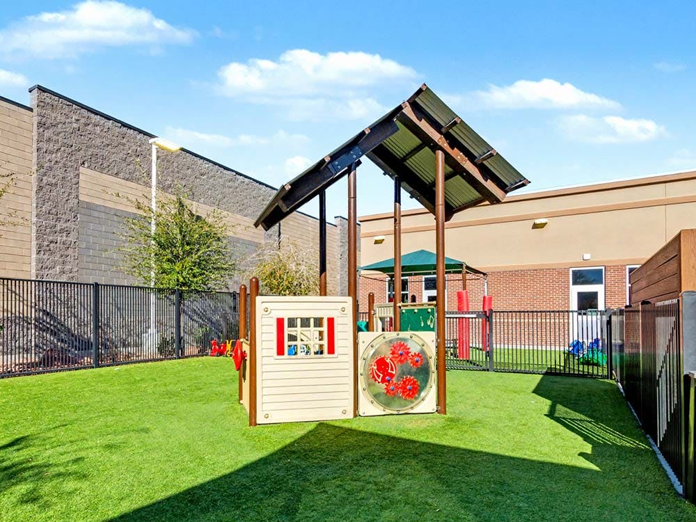 A children's playground with artificial turf, a small playhouse, and sunshade