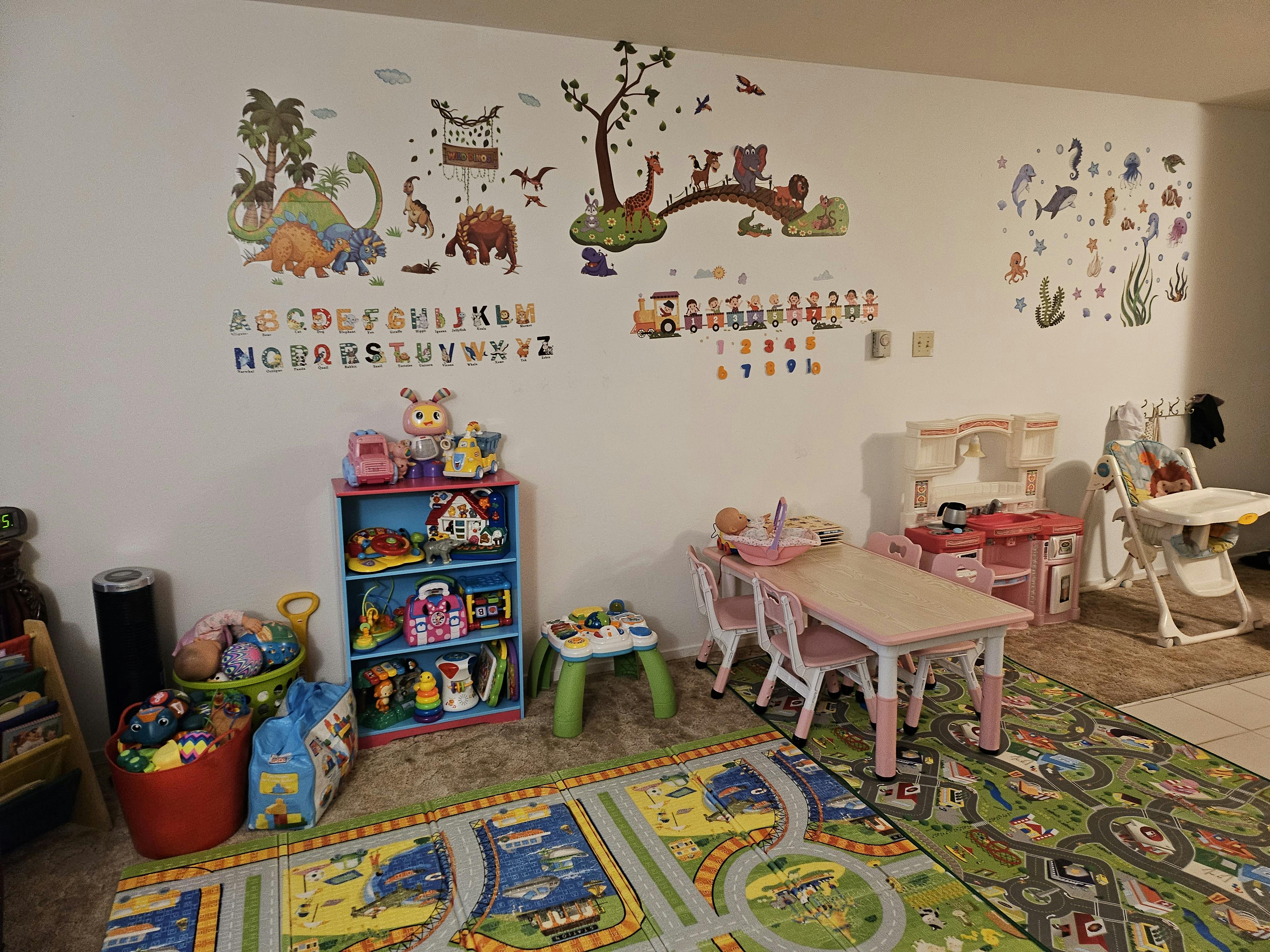 Playroom with wall decals, toy shelf, small table and chairs, and play mat