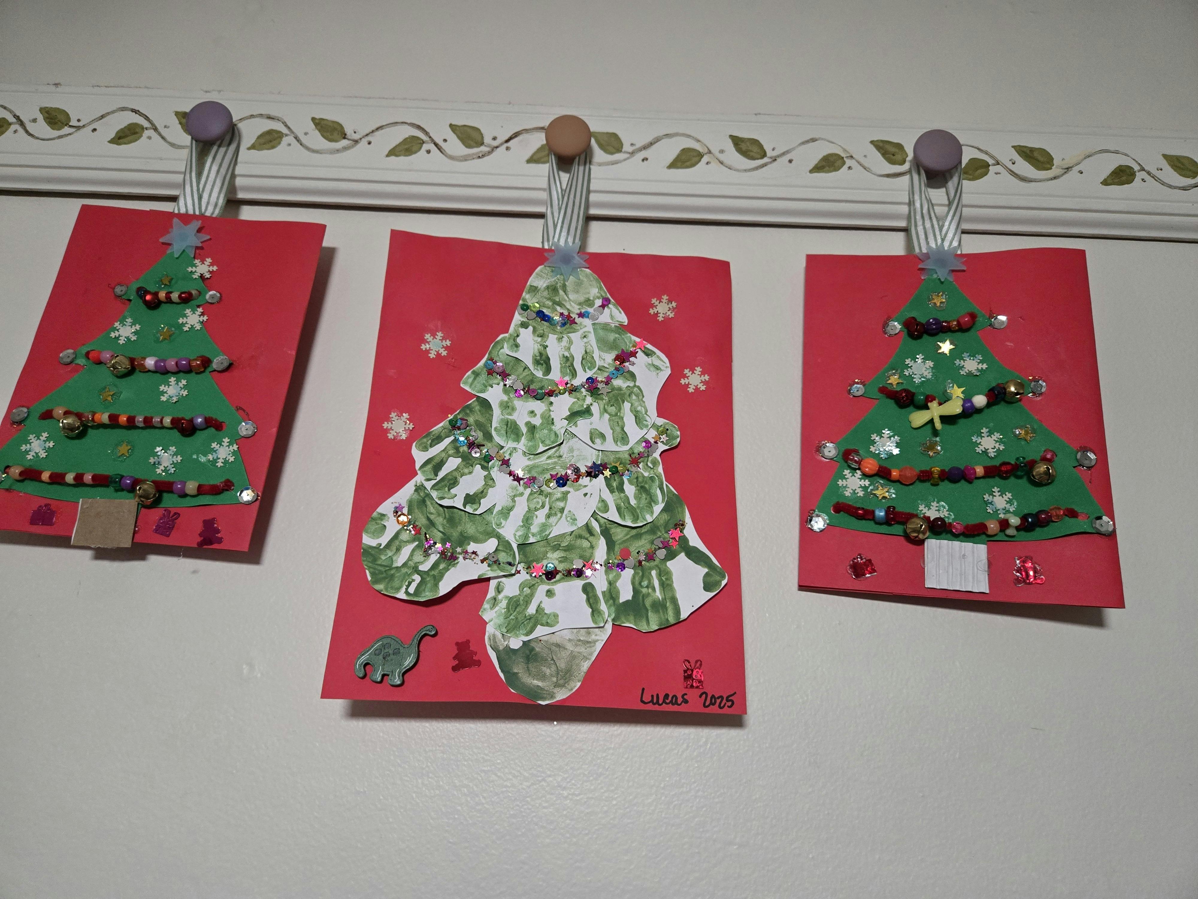 Three handmade Christmas tree crafts hanging on a wall
