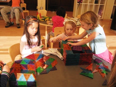 Three children playing with colorful magnetic tiles at a table