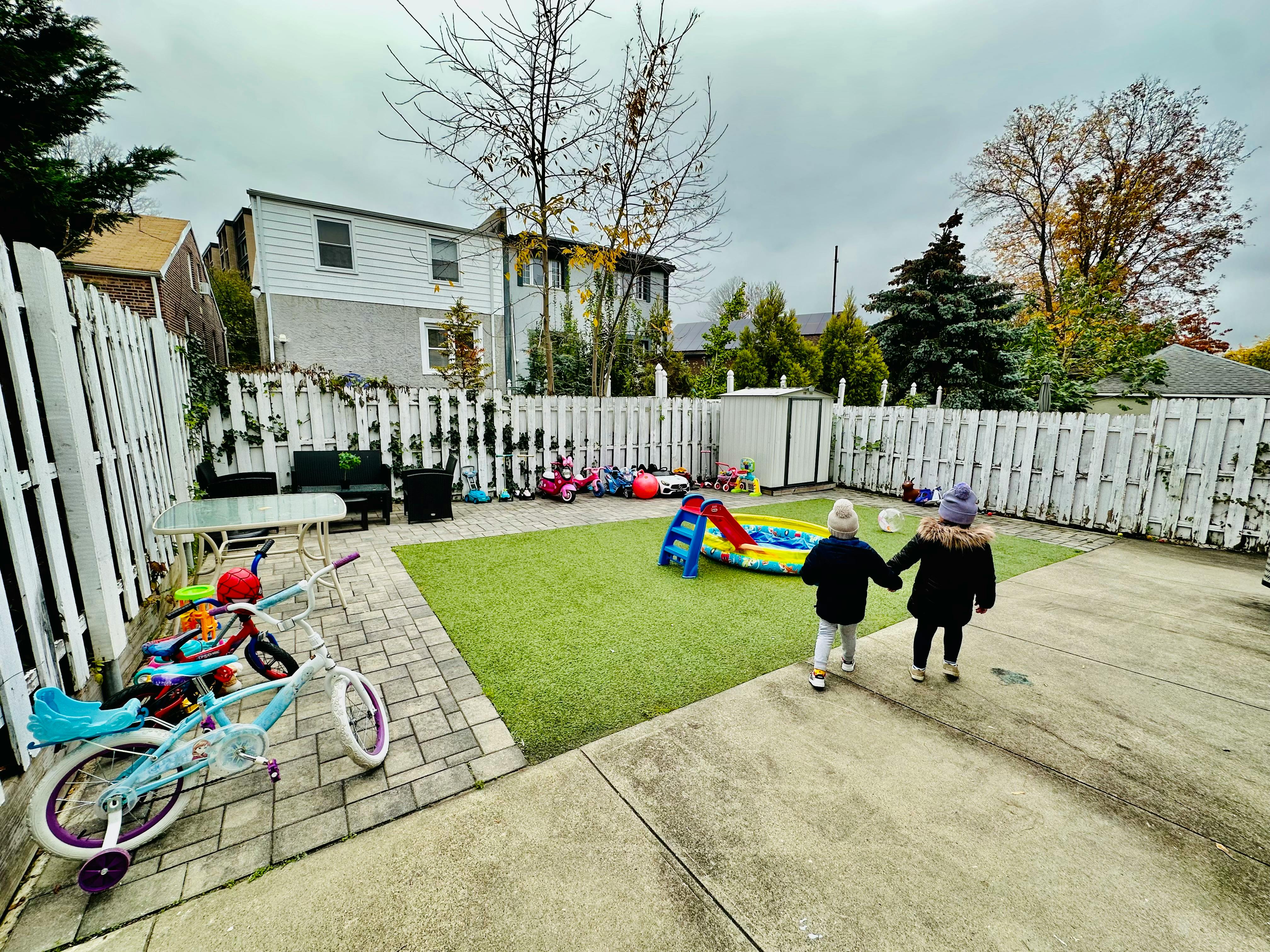 Two children holding hands walking towards a play area in a backyard