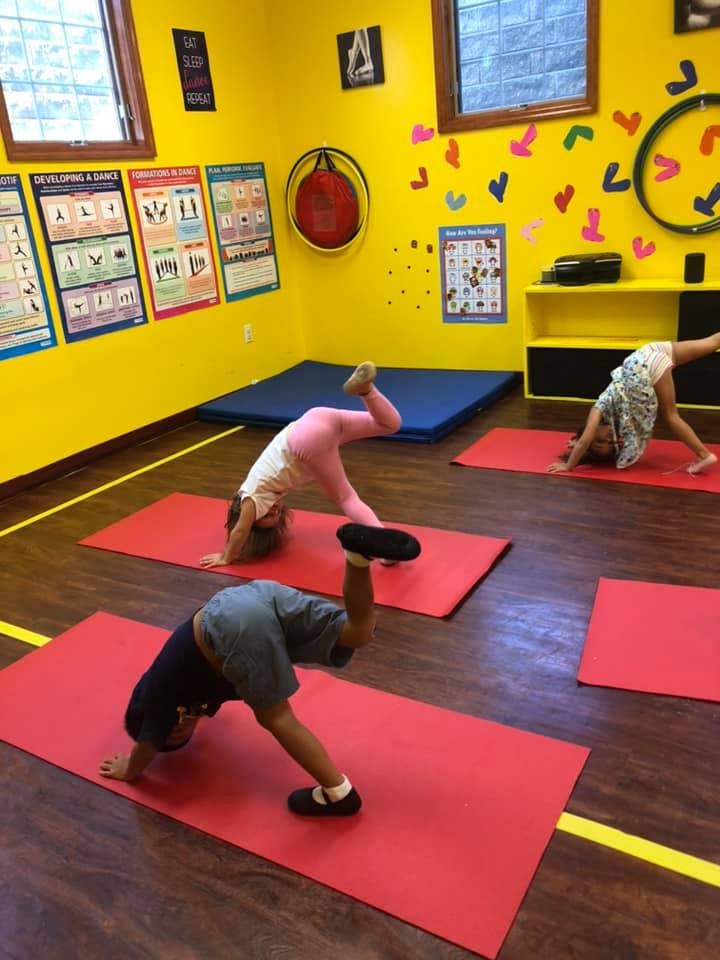 Three children doing yoga poses on red mats in a room