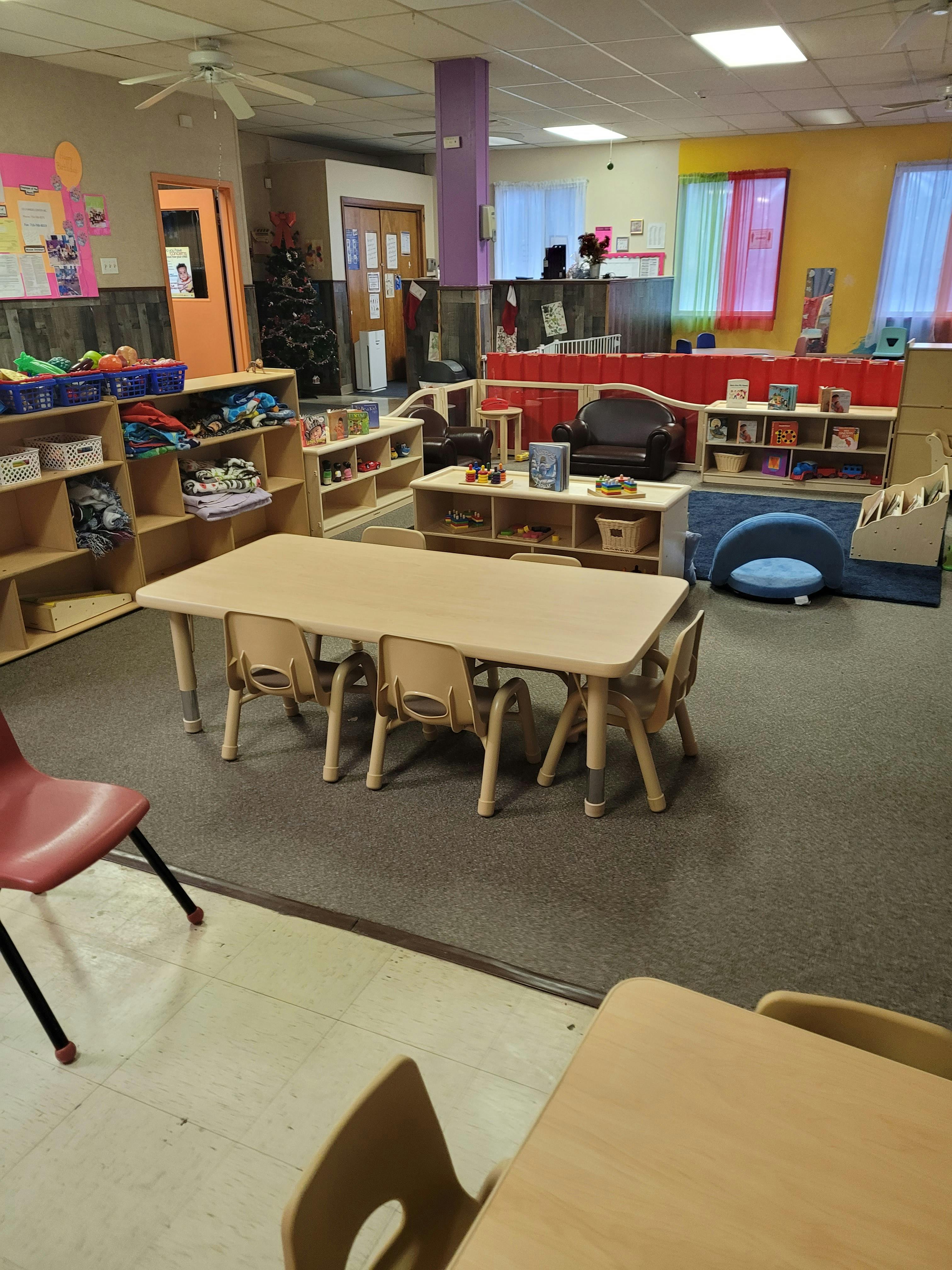 Classroom with small tables and chairs, shelves with toys and books