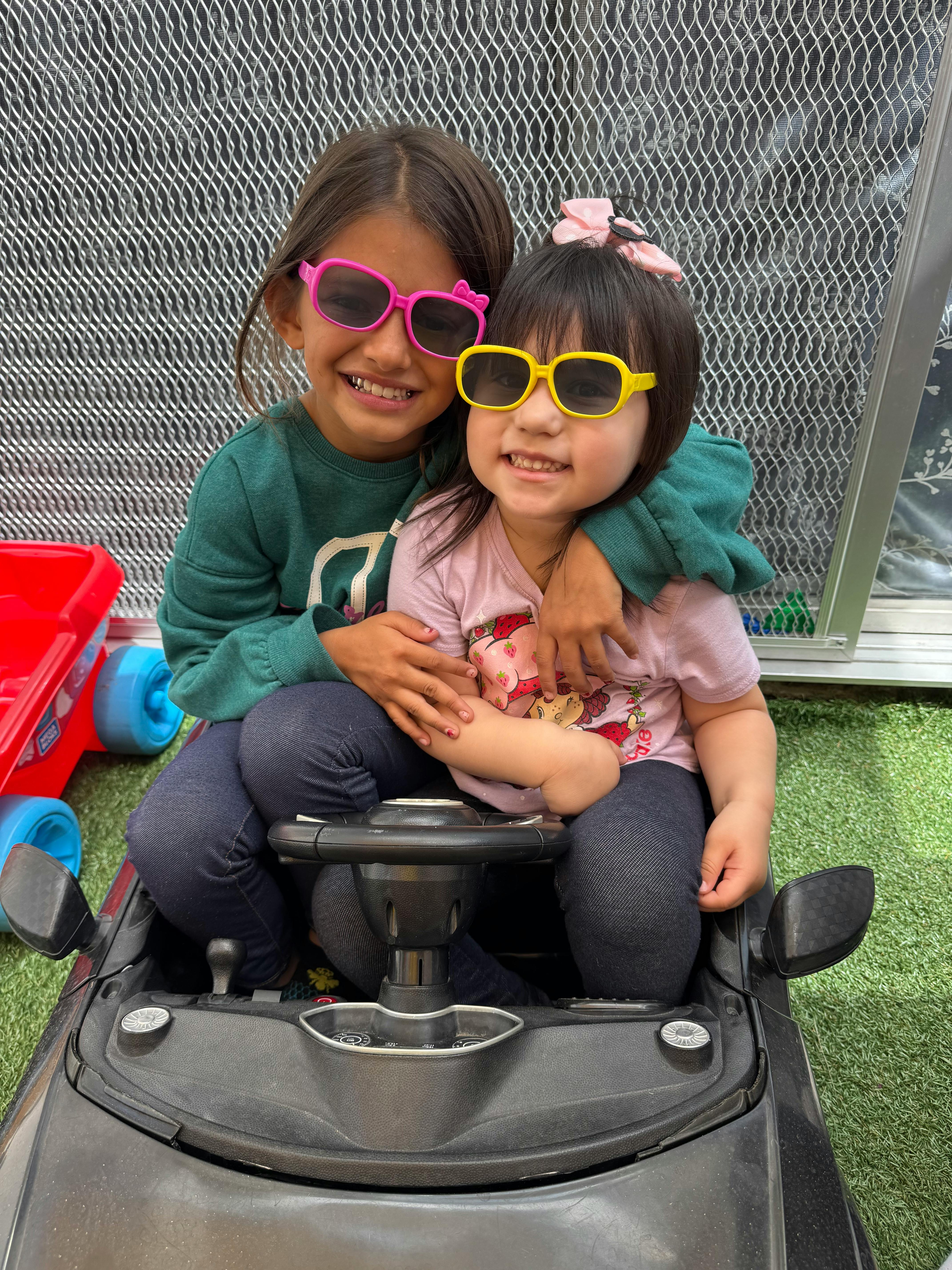 Two children wearing sunglasses sitting in a toy car