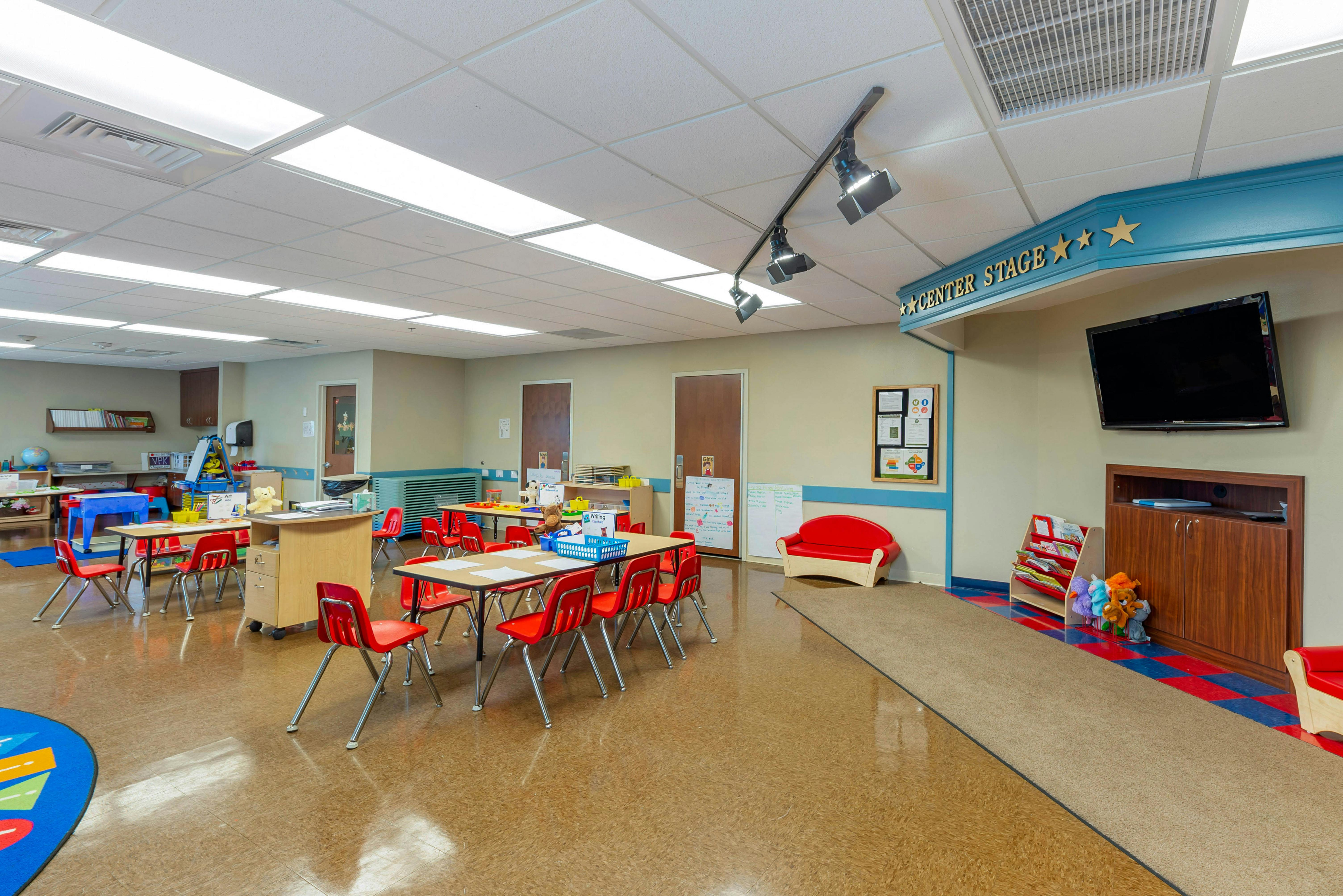 Empty classroom with small tables and red chairs, ready for students