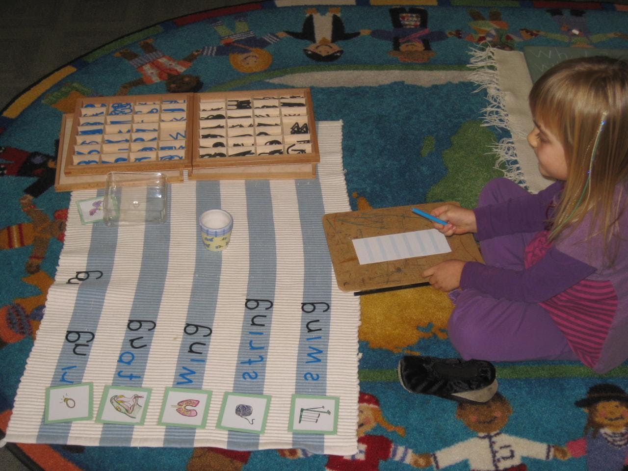 Child on floor working with word cards and a wooden box of small objects