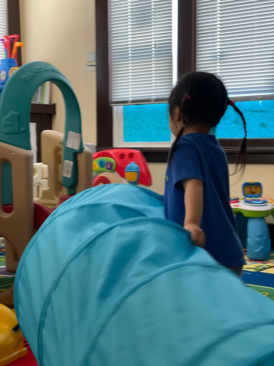 Child standing next to a blue play tunnel