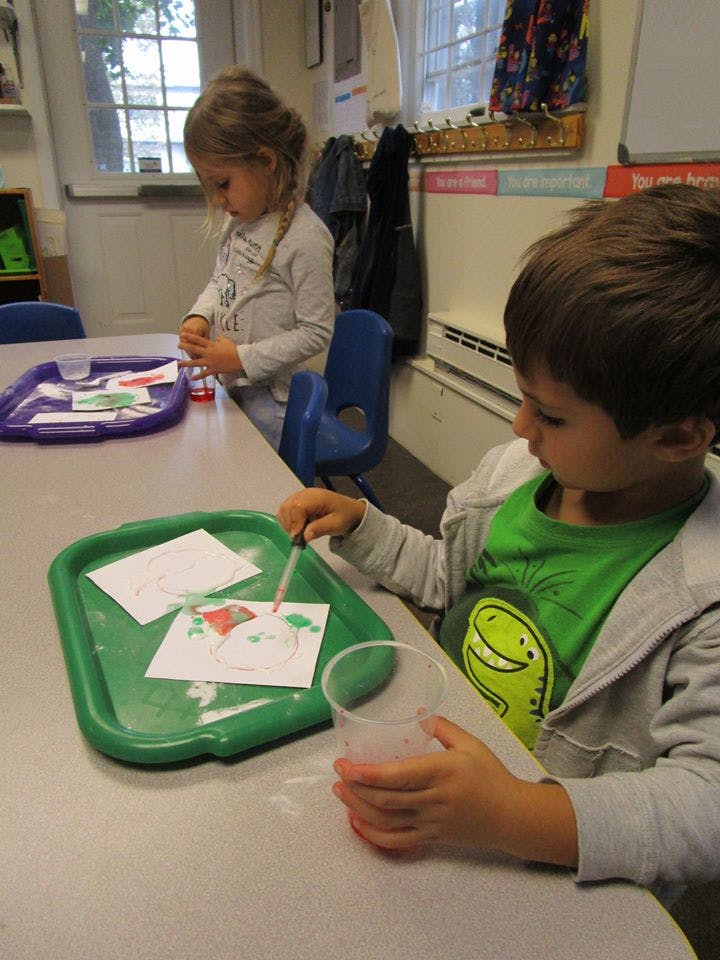 Two children at a table, one using a dropper on paper, the other looking down