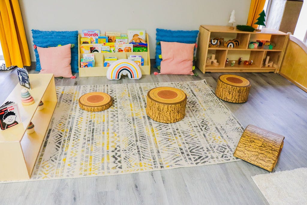 Children's play area with a rug, cushions, books, and wooden stools