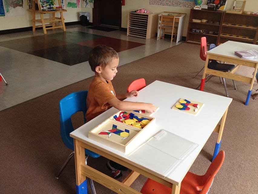 Child playing with a puzzle at a table in a classroom