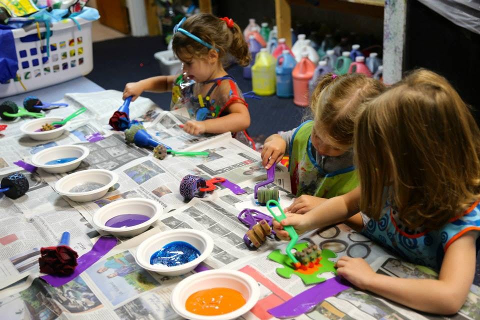 Three children painting at a table with bowls of paint