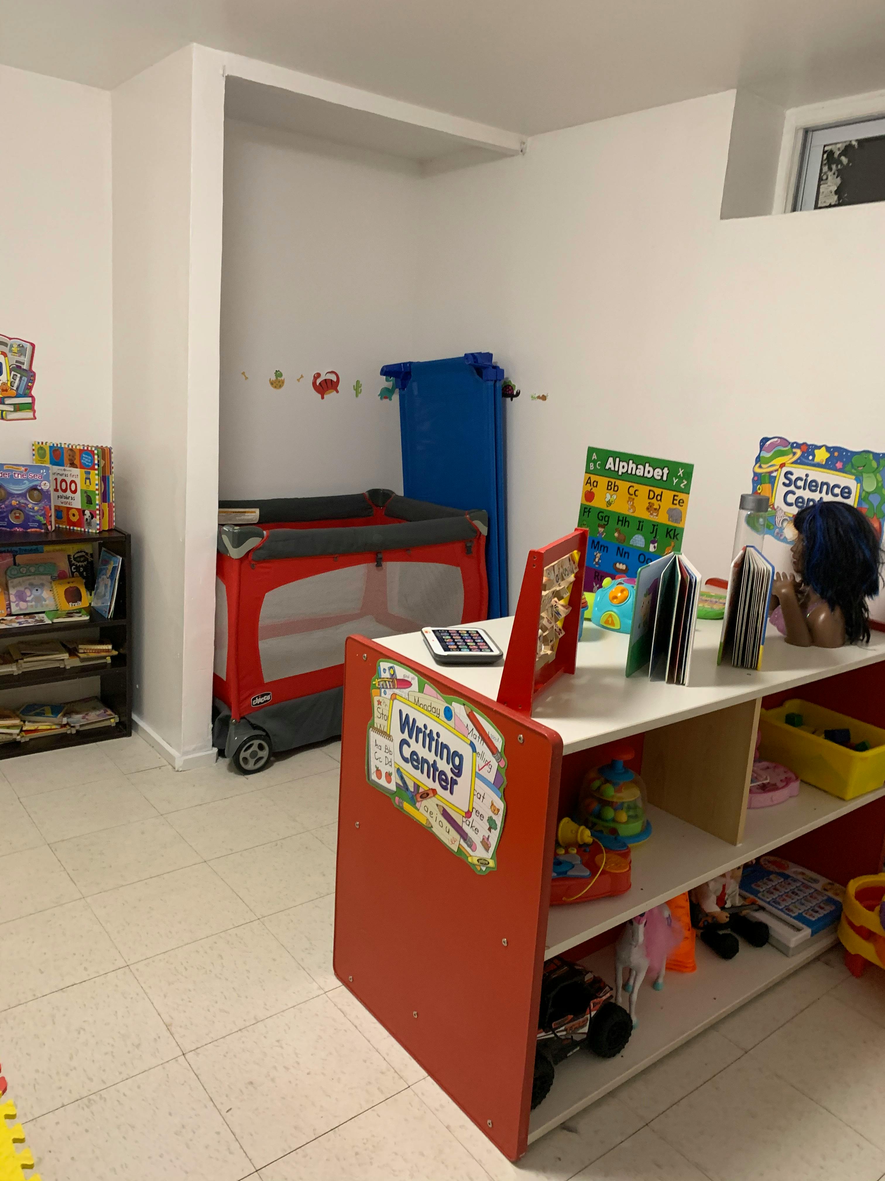A classroom with a red playpen, a writing center, and shelves with books and toys