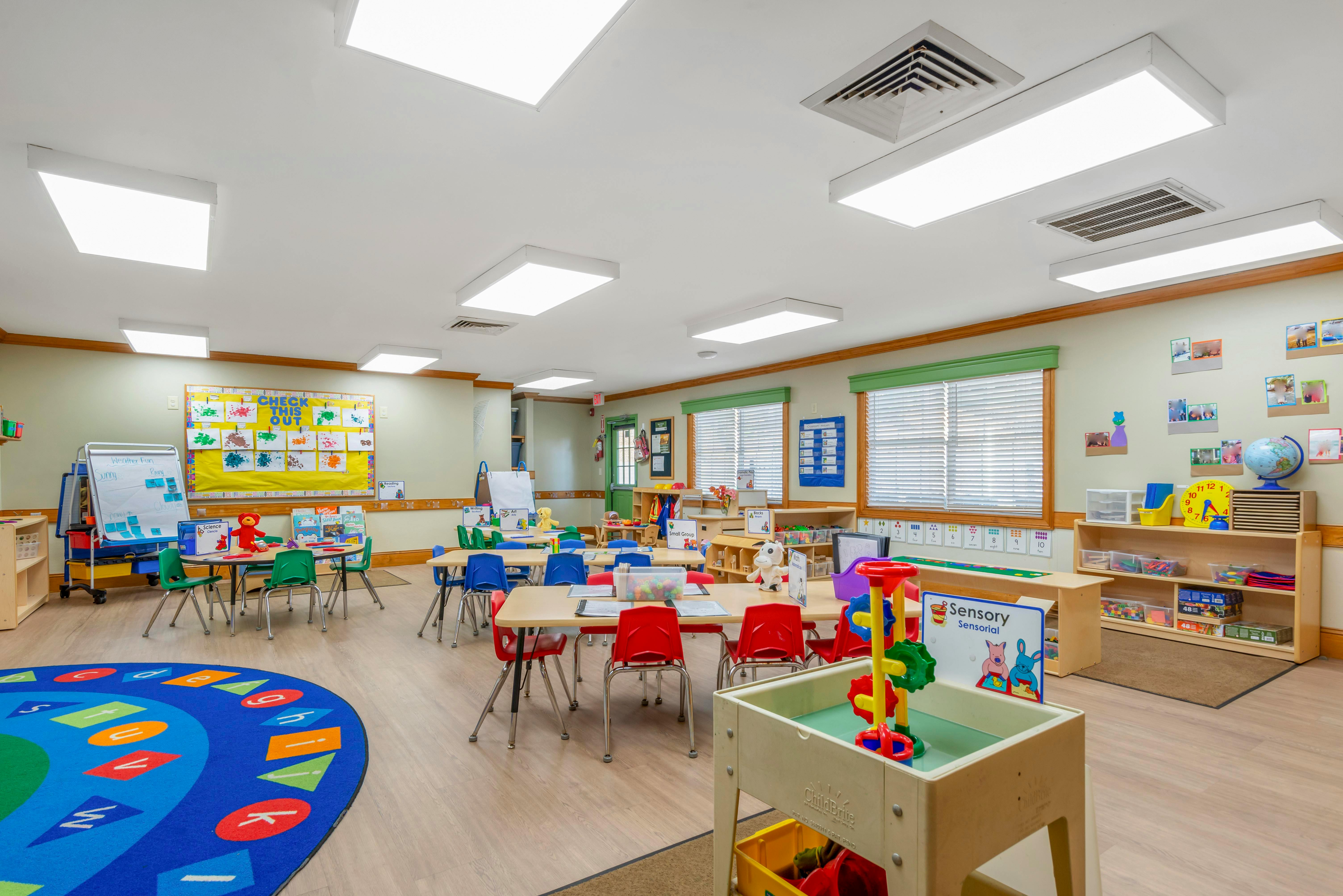 Colorful classroom with tables and chairs, a large rug, and educational displays