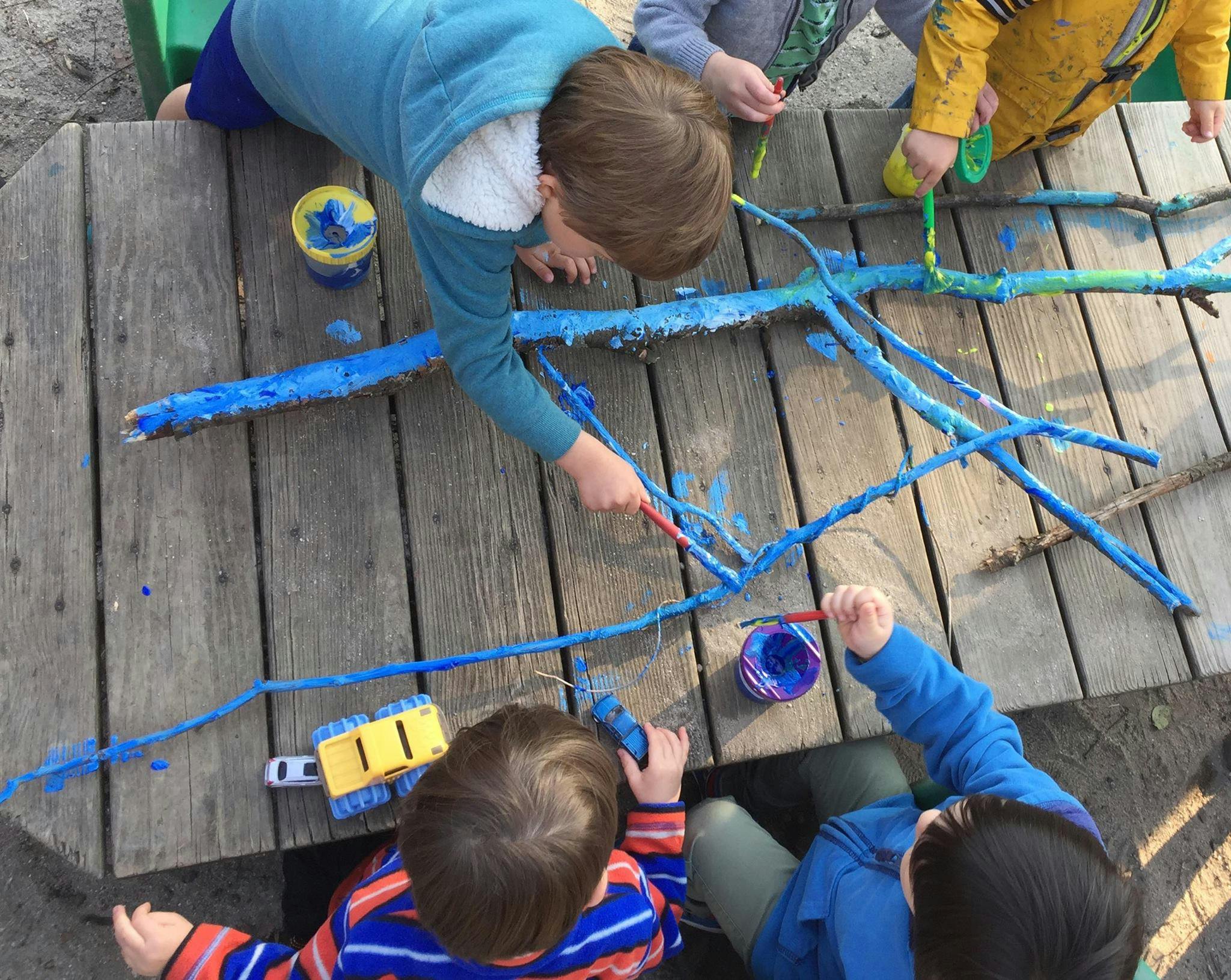 Children painting sticks blue on a wooden surface