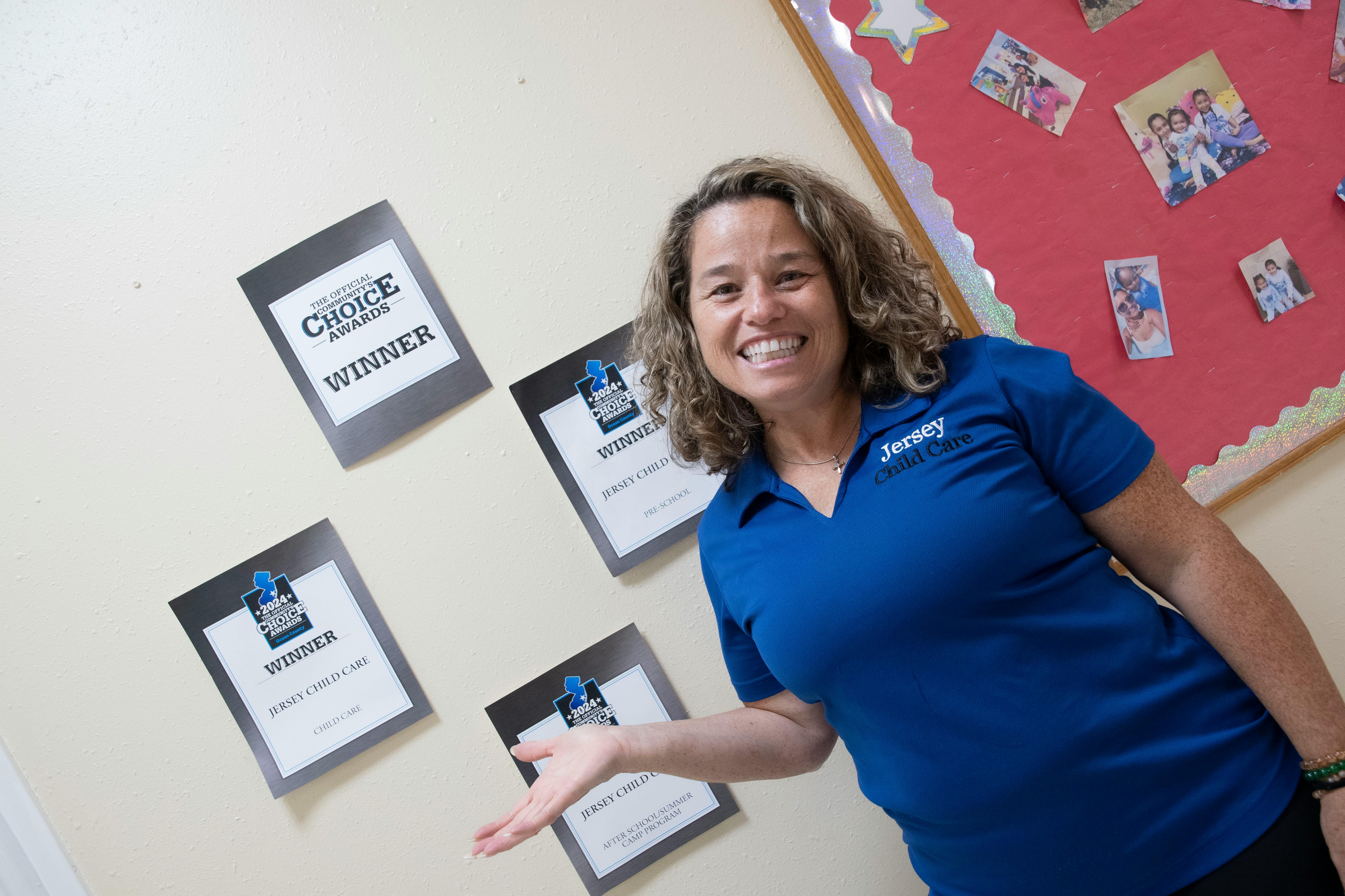 Person in blue shirt gesturing towards awards on a wall