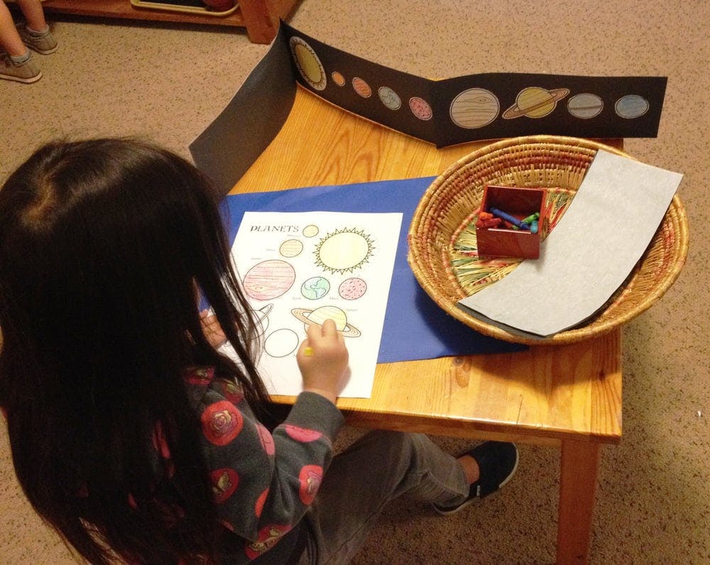 Child coloring a picture of planets at a table