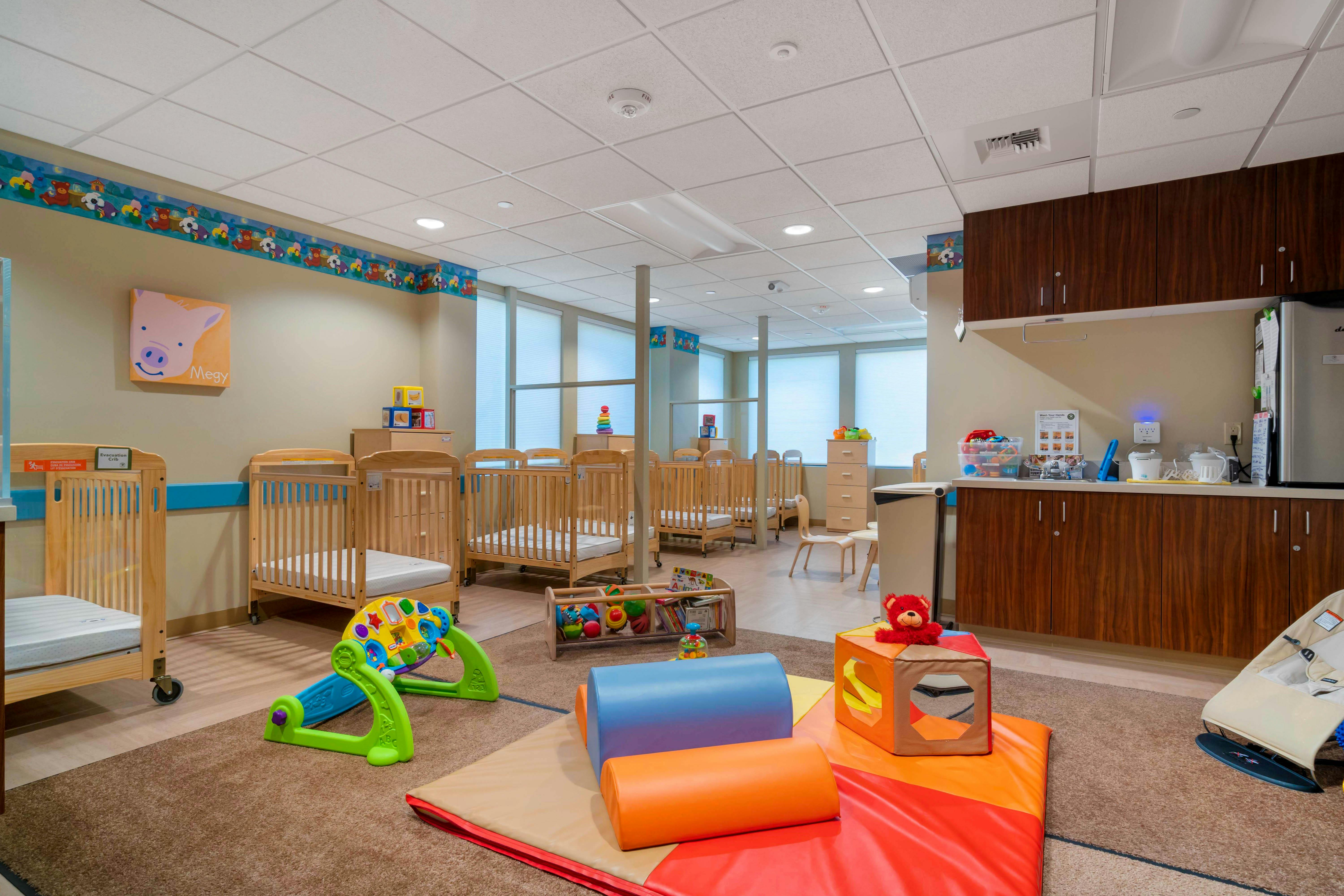 Baby room with multiple cribs, playmats, and toys