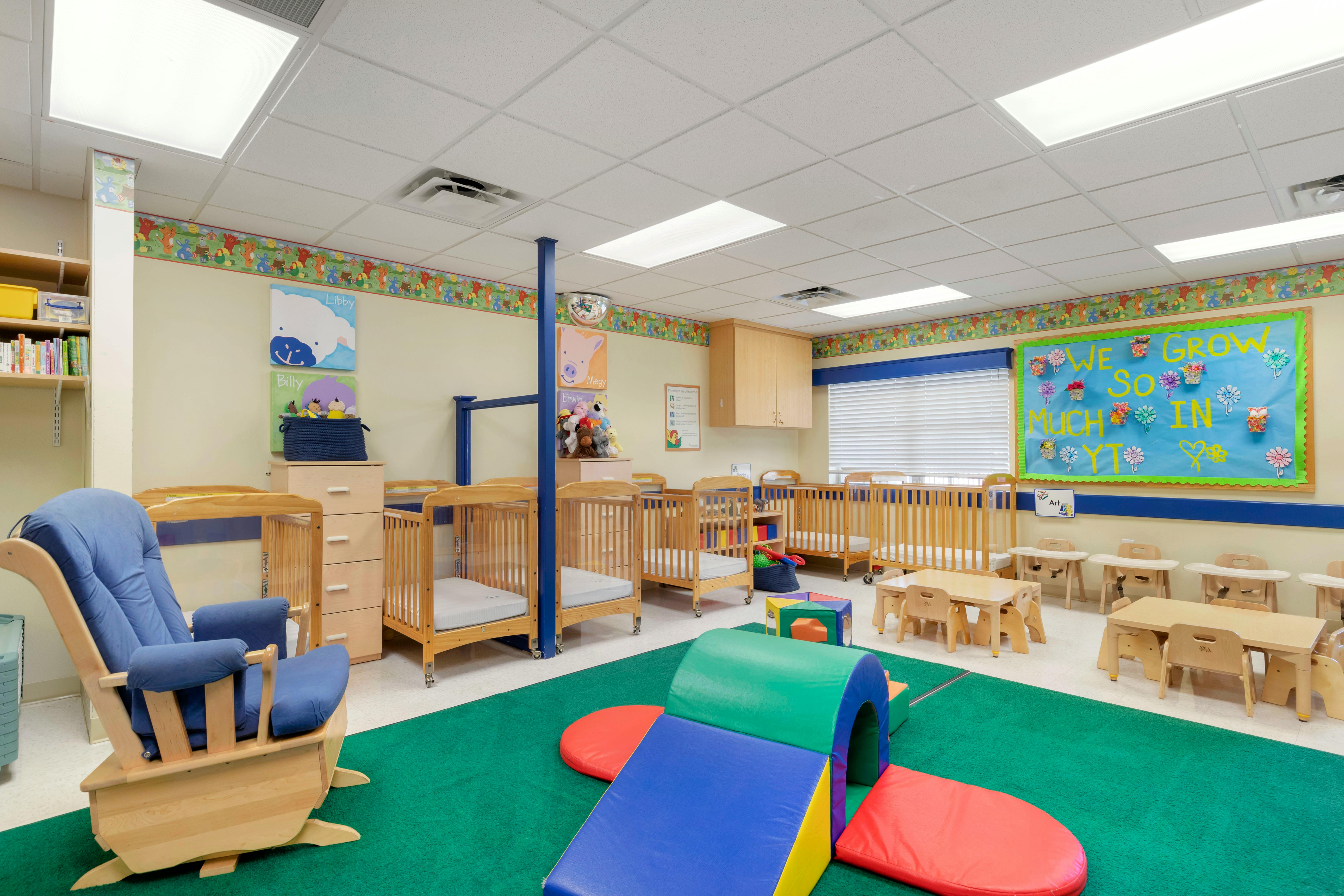 Cribs, small tables, and play mats in a bright daycare room