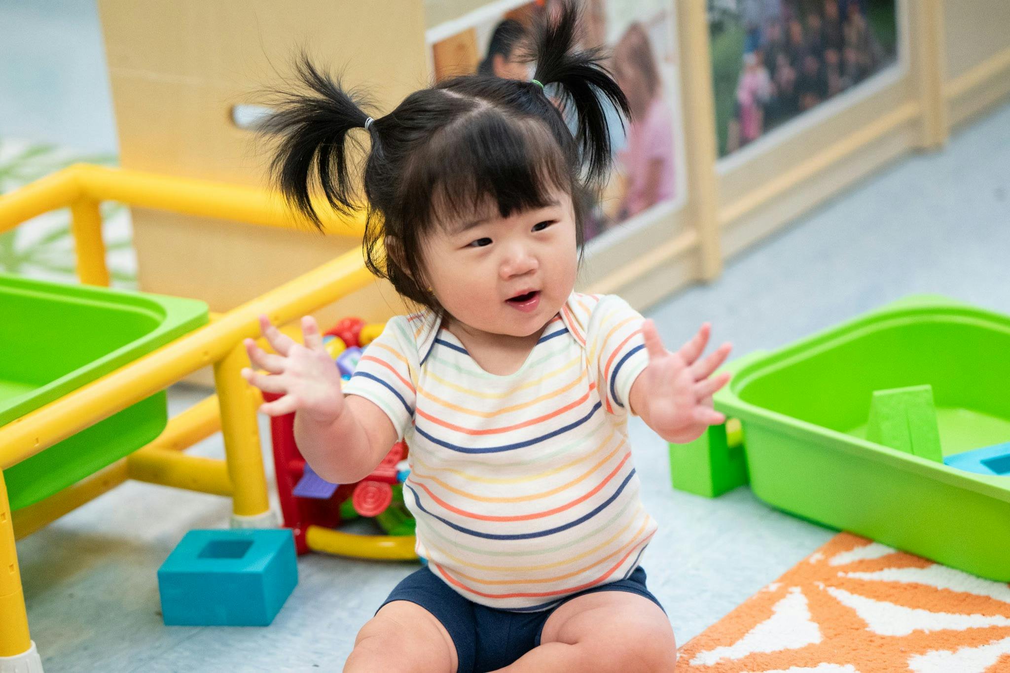 Child with pigtails sitting on the floor with hands raised