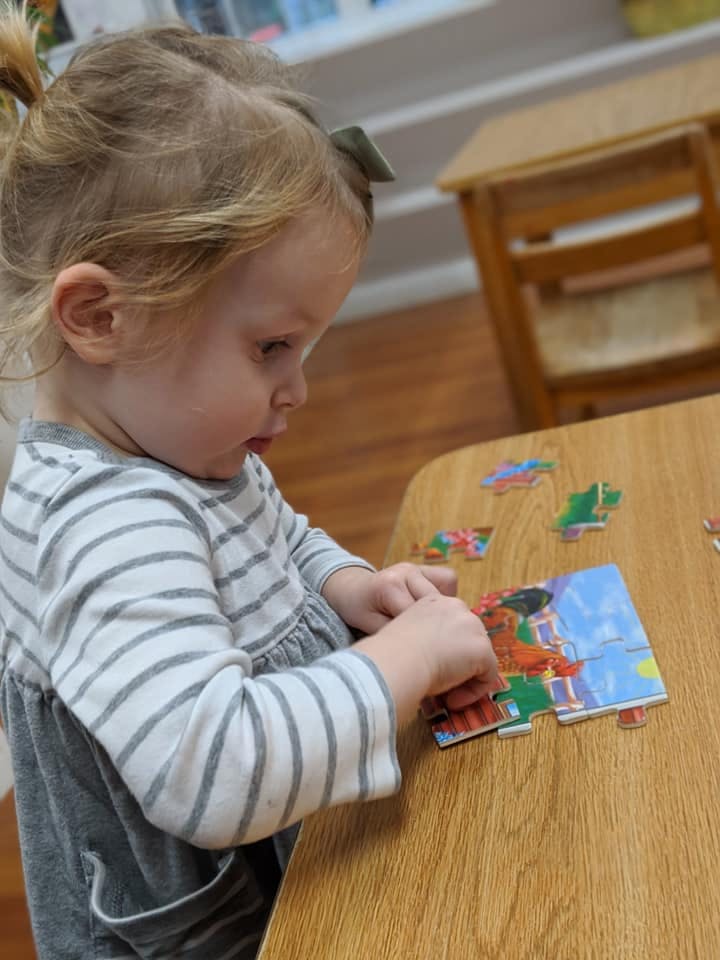 Child assembling a puzzle on a wooden table
