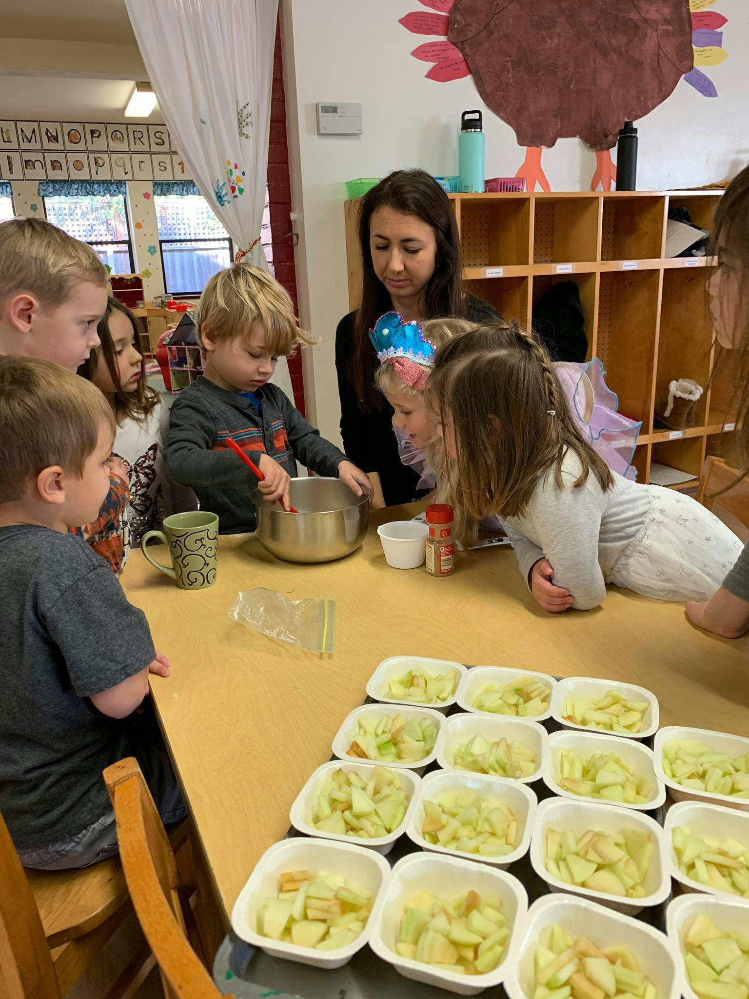 Adult and children gathered around a table with bowls of chopped apples