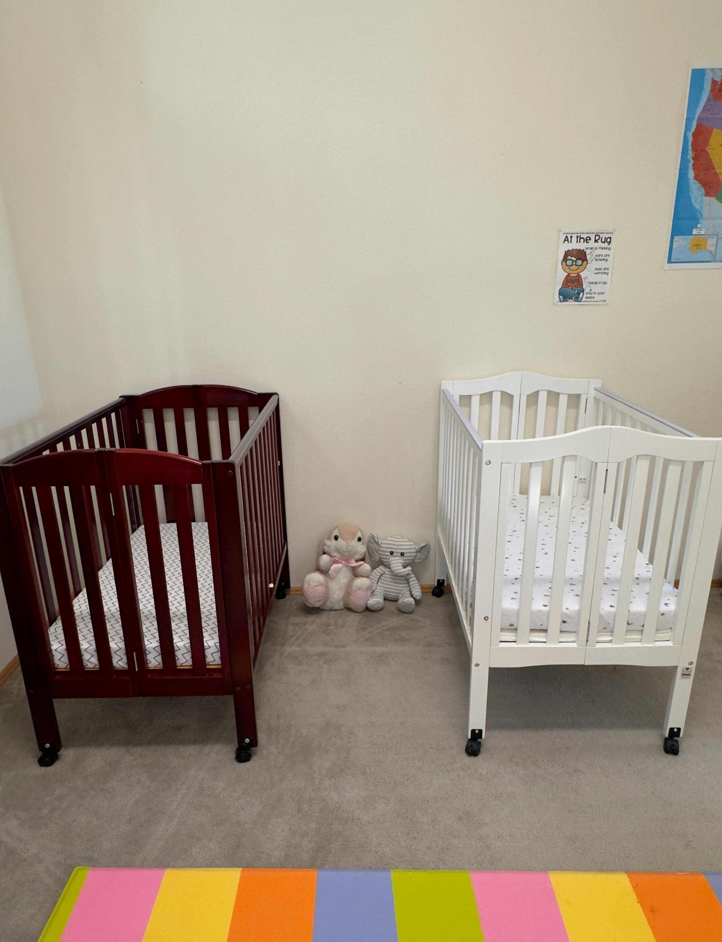 Two cribs, one dark wood and one white, with stuffed animals between them