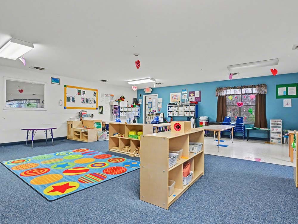 Colorful classroom with blue carpet, tables, and shelves of materials