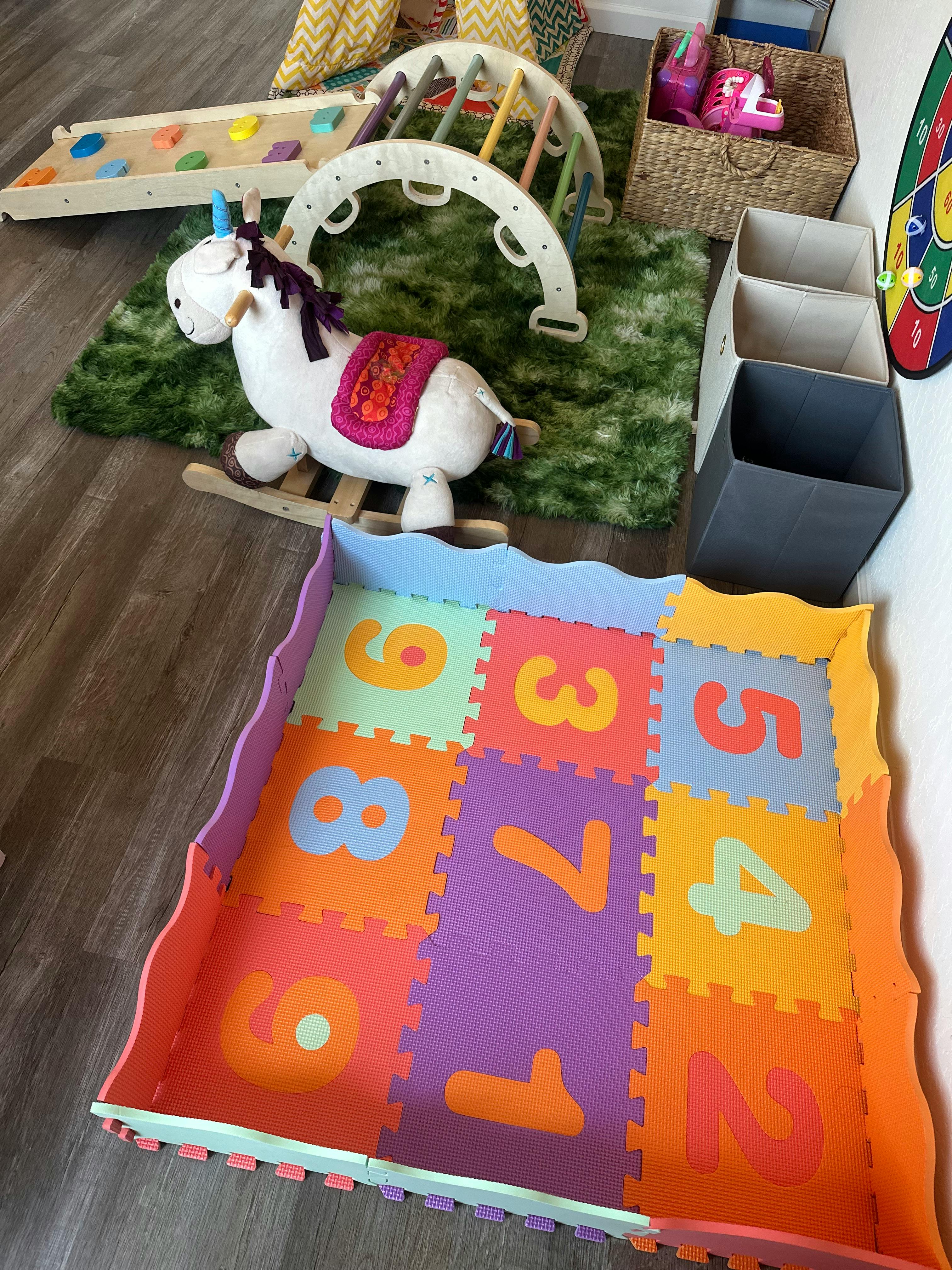 Playroom with foam number floor mats, a rocking unicorn toy, and climbing gym